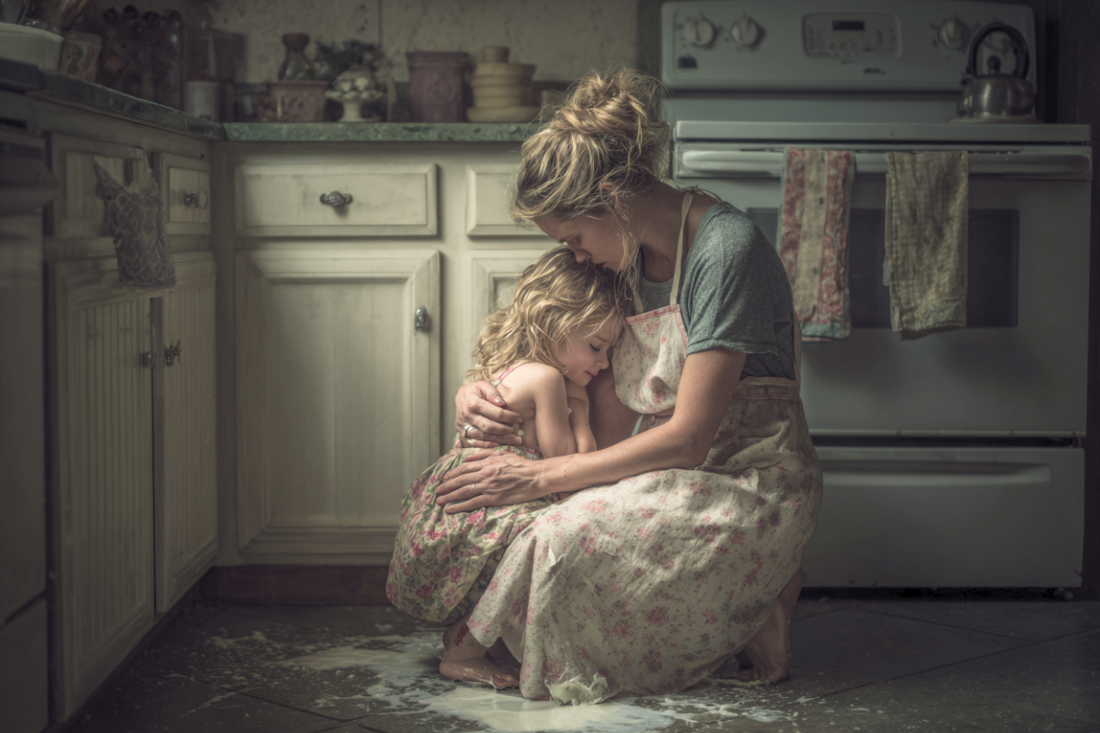Mother comforting her young child after spilling milk on the kitchen floor, showing patience and compassion in a difficult moment